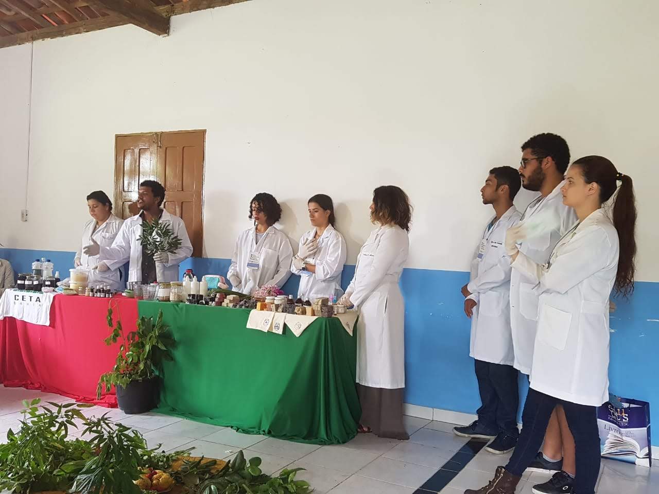 Alunos de jaleco branco estão em pé falando sobre a oficina